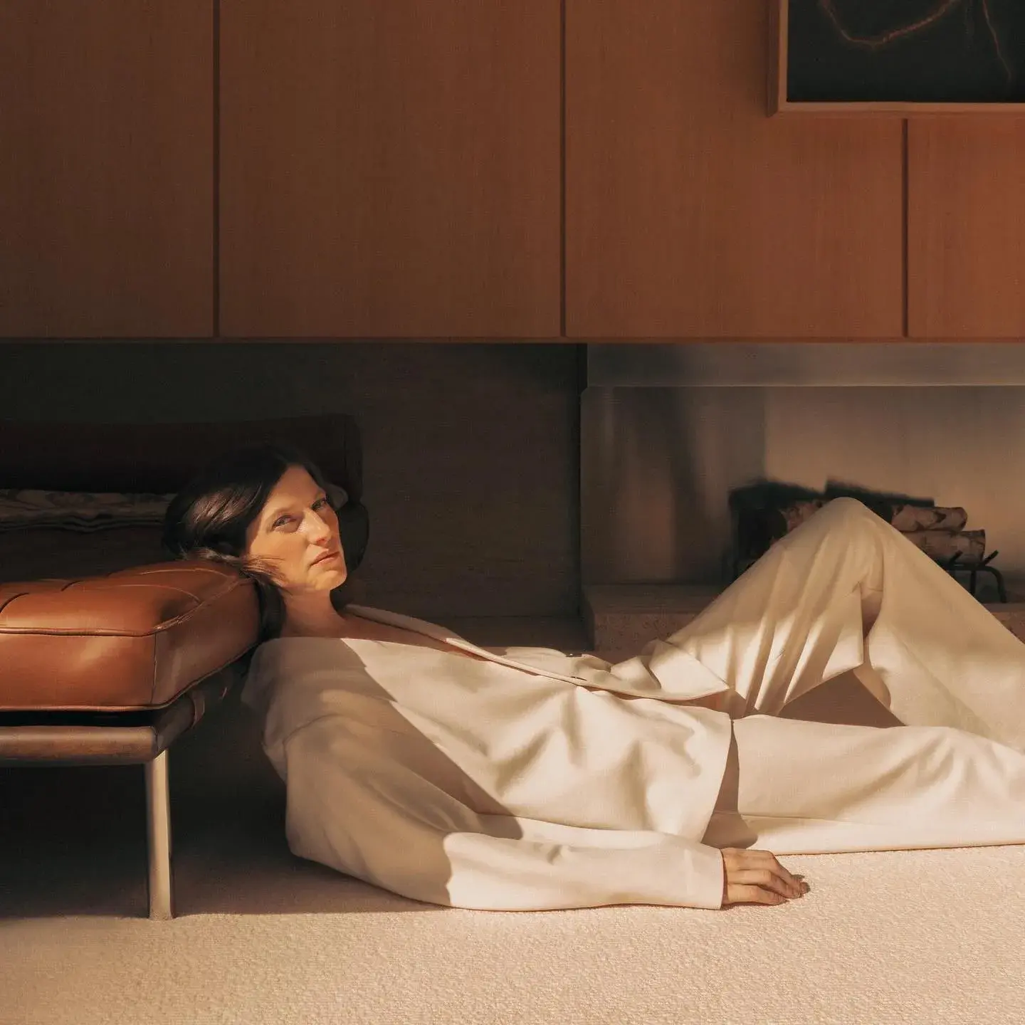 A model reclining in a cream suit on a pale carpet in low sun