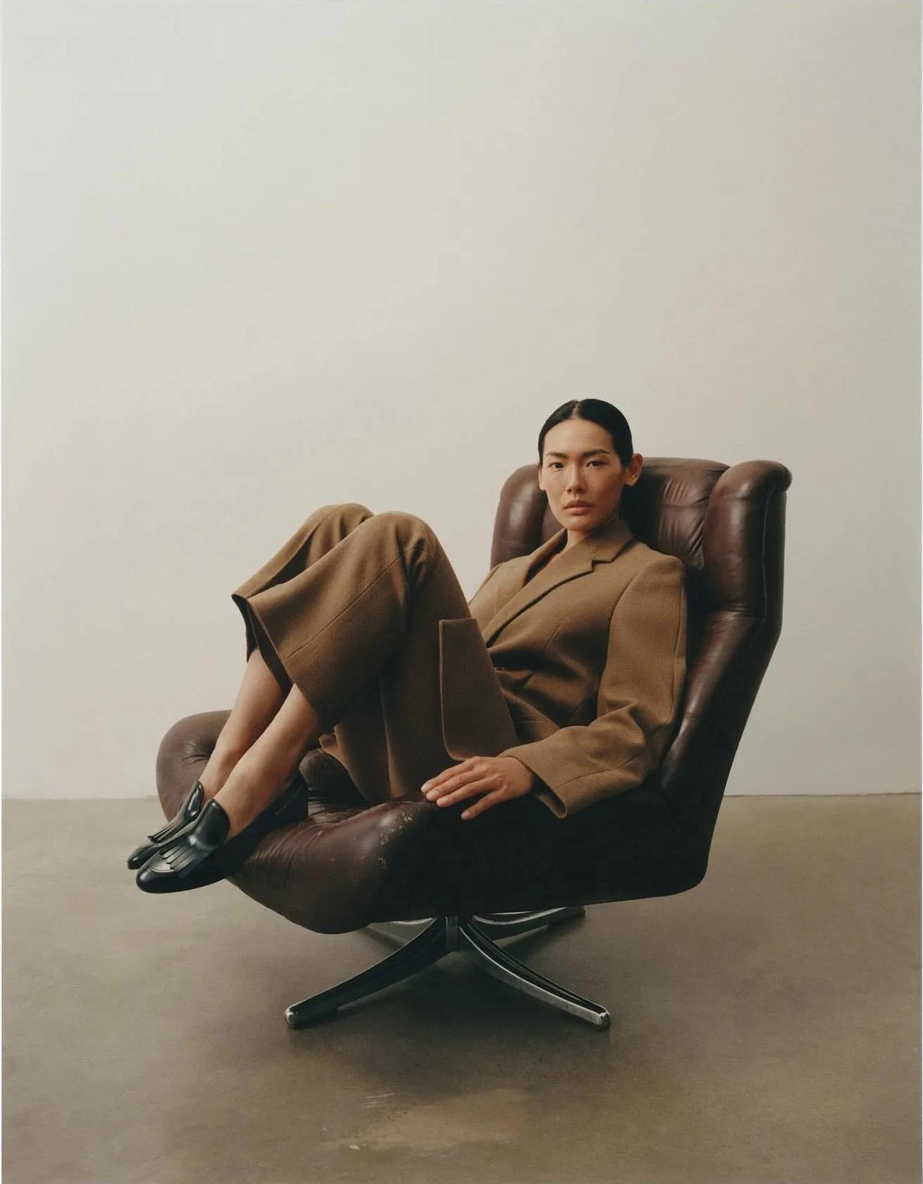 A model in a brown wool suit seated in a leather swivel chair