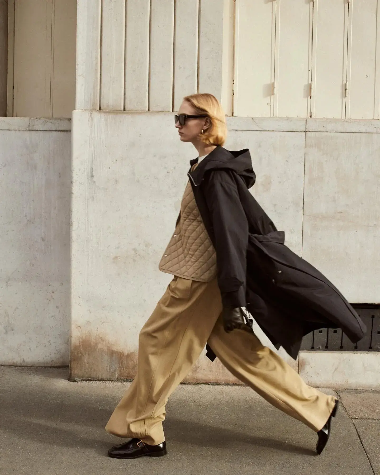 A model walking in a black hooded coat over tan wide-leg trousers