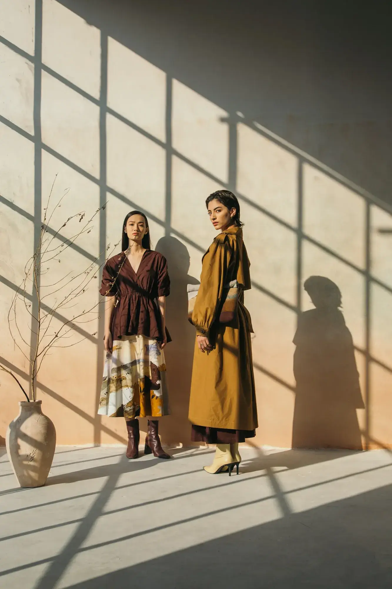 Two models against a sunlit wall in burgundy and ochre