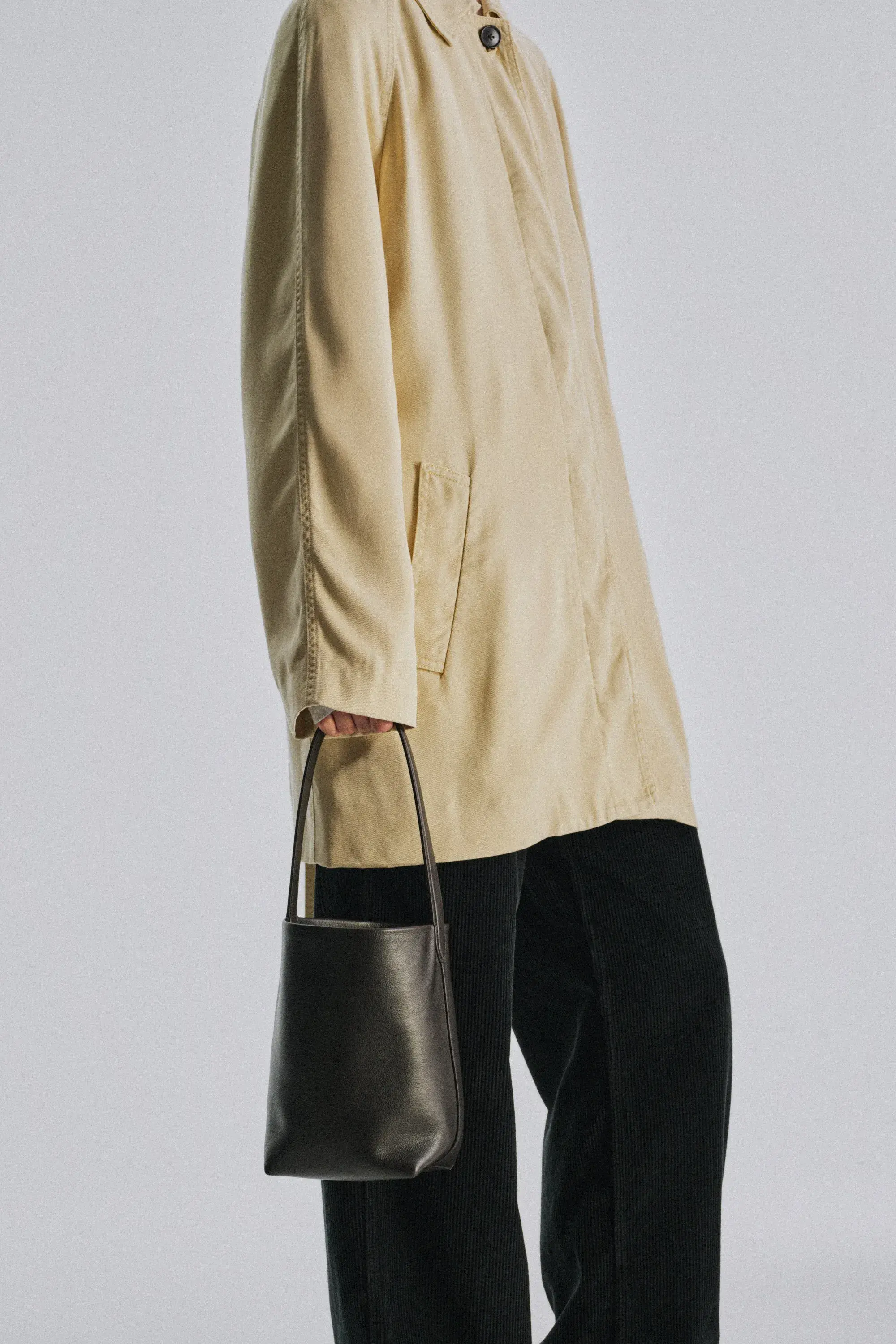 A small black leather bucket bag carried at the hip against a pale cotton coat